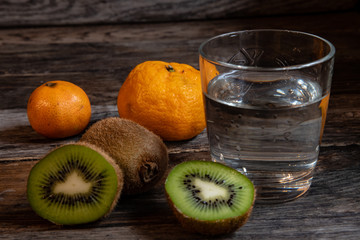 Mandarin, kiwi, a glass of water on a background of old boards, on an old rustic table.