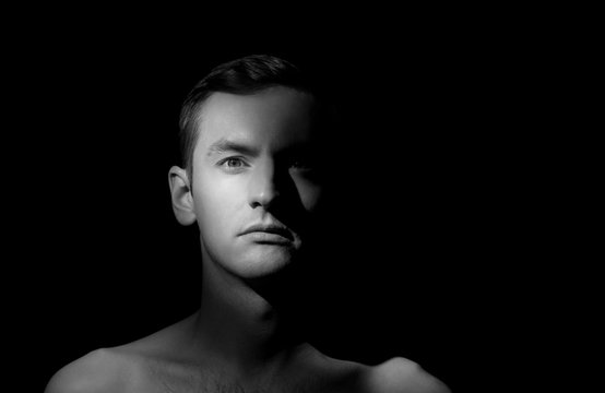 black and white dramatic portrait of a guy close-up on a black background with one light source