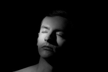 black and white dramatic portrait of a guy close-up on a black background with one light source
