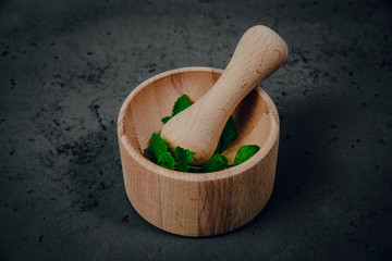 Wooden mortar with herbs on stone background. The concept of crushing and crushing spices, herbs. Preparation of ointments, creams. Caring for health, natural methods of obtaining medicines.