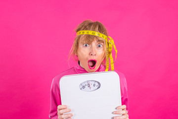 woman with weighing scale and measuring tape with expression of effort and difficulty on colored background