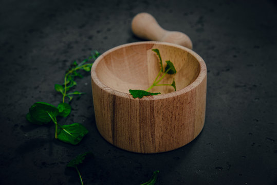 Wooden mortar with herbs on stone background. The concept of crushing and crushing spices, herbs. Preparation of ointments, creams. Caring for health, natural methods of obtaining medicines.