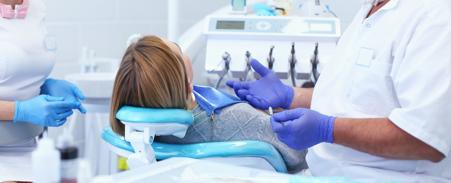 Senior male dentist in dental office talking with female patient and preparing for treatment