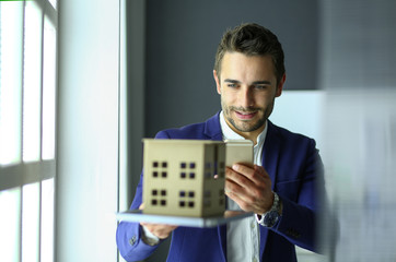 Businessman holding house miniature on hand standing in office.