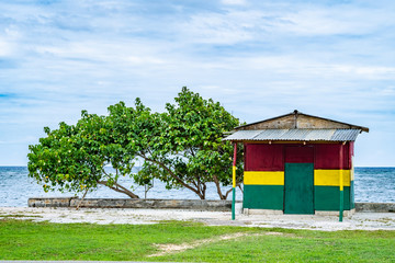 Small colorful wood/ wooden/ board/ plywood building painted in red, green, gold rasta colors, by the seaside. Traditional Caribbean island countryside shop/ bar/ restaurant architecture by the ocean.