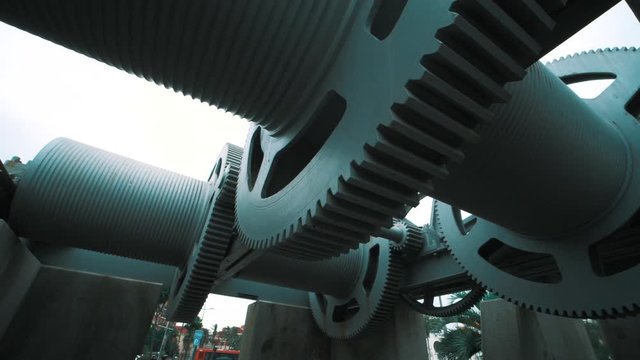 Looking up below the wheels of an industrial crane, slow motion panning shot. The giant cogs fill the foreground of the shot.