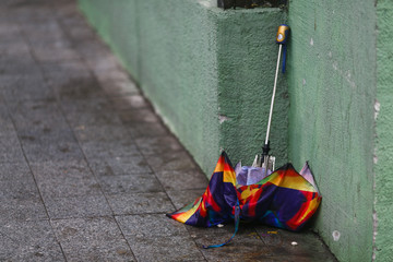 Close-up. A broken multi-colored umbrella lies against the wall of the building in windy rainy weather. Thrown out umbrella.