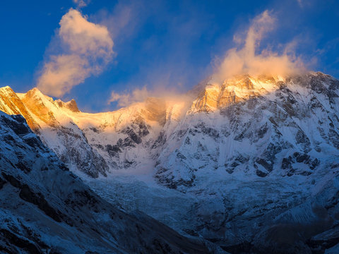 Snow-covered Annapurna South glows in warm sunrise light above a rugged Himalayan valley in Nepal