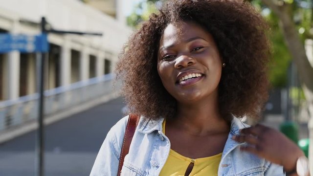 Portrait of young african american woman with curly hair smiling and looking at camera. Black curvy girl in casual clothes enjoying outdoor. Pretty black college student in campus.