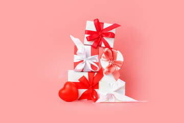 White gift boxes with red satin ribbons on a pink background. Festive presents for St. Valentine's Day, International Women's Day, wedding or engagement.