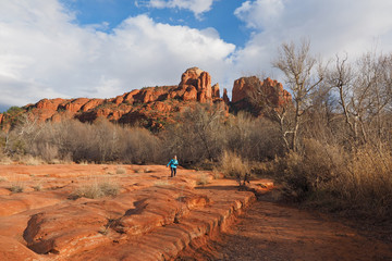 Woman in blue jacket photographing Cathedral Rock under winter cloudscape in Red Rock State Park outside of Sedona Arizona.