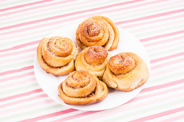 Obraz na płótnie Canvas Freshly baked homemade snail buns with sugar and cinnamon on white plate and striped tablecloth. Balanced nutrition, proteins and carbohydrates, cereals
