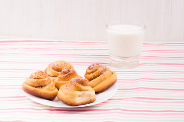 Freshly baked homemade snail buns with sugar and cinnamon on white plate and striped tablecloth with milk in glass. Balanced nutrition, proteins and carbohydrates, cereals