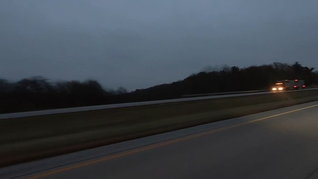 2X, POV through drivers side window while driving red vehicle down an interstate highway at dusk on a rainy, cloudy day; point of view