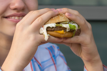 teenager eating a delicious juicy big burger, close-up