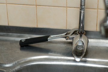 An adjustable spanner lies on a rusty kitchen faucet. Incomplete repair process