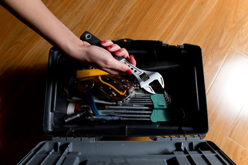 girl with red manicure takes an adjustable wrench from a tool box