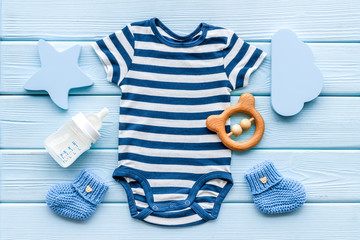 Blue bodysuit for baby boy near children's accessories on blue wooden background top-down