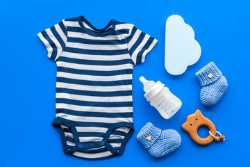 Blue bodysuit for baby boy near children's accessories on blue background top-down