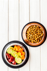 Healthy feed for cats and dogs. Bowls full of dry feed, meat and vegetables on white wooden background top-down copy space