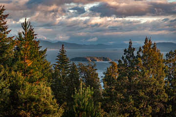 Beautiful cloudy sunset view of the lake Nahuel Huapi, its islands and mountains in the background, surrounded by forests in Bariloche, Argentina - Powered by Adobe