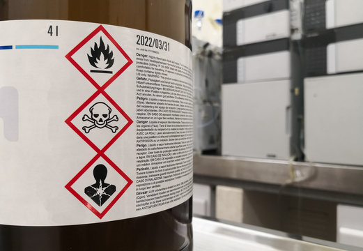 Chemical substance in a laboratory. Amber glass bottle. Tagged with GHS symblogy with toxicity, flammability and death warnings. Liquid chromatography equipment.