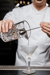 Bartender pouring a cocktail from a mixing glass into a martini glass