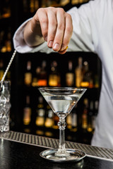 Bartender prepairing a cocktail at the bar, squeezing a lemon peel over a drink in a martini glass
