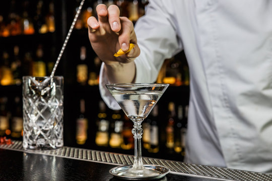 Bartender prepairing a cocktail at the bar, squeezing a lemon peel over a drink in a martini glass