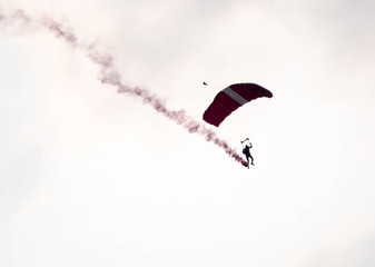 silhouette parachute stunt unfocused and blurry while gliding in the air with red smoke trail during an air exhibition
