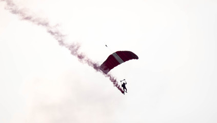 silhouette parachute stunt unfocused and blurry while gliding in the air with red smoke trail...