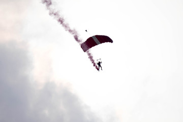 silhouette parachute stunt unfocused and blurry while gliding in the air with red smoke trail...