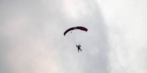 silhouette parachute stunt unfocused and blurry while gliding in the air with red smoke trail during an air exhibition