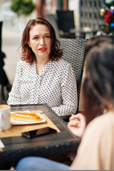 Frowning shocked elegant woman listening to story of her friend when meeting with her in outdoor cafe