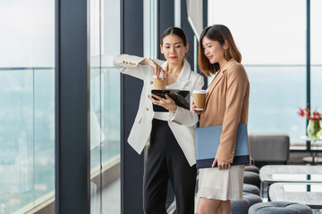 Two asian businesswomen talking during coffee break in modern office or coworking space, coffee...