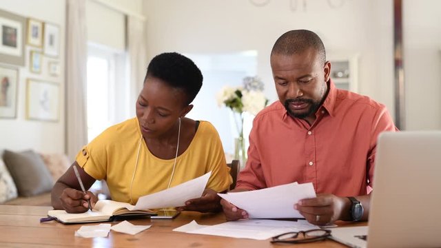 Cheerful mature couple sitting and managing expenses at home. Happy african man and woman paying bills together and managing budget. Black smiling couple checking accountancy and bills.