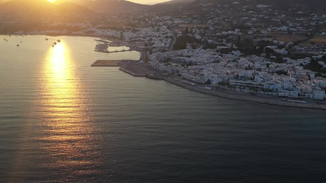Drone tilt reveal of amazing warm sunrise overlooking whitewashed town on Paros Island