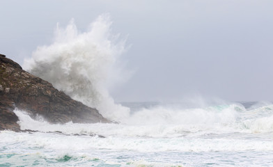In winter on a beach near the port city of Finisterre in Galicia in northern Spain. Seven meter high Atlantic waves meet rocks and the sandy beach. The air is full of haze.