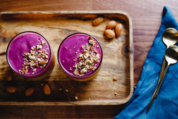 Top view of two glasses with violet berry smoothie are served crushed almond on a wooden tray.