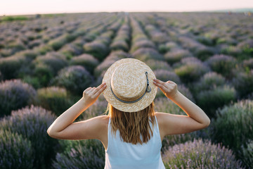 A girl holds her hat with her hands and looks at a field of lavender
