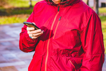 A man in a red waterproof sport jacket stands on the street and looking his phone. Sportsman....