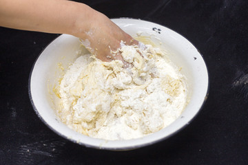 Hands of the cook prepare the dough for bread on a black background. Restrained shot with flour.