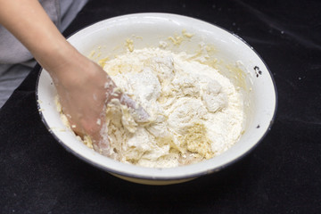 Hands of the cook prepare the dough for bread on a black background. Restrained shot with flour.