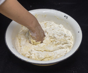 Hands of the cook prepare the dough for bread on a black background. Restrained shot with flour.