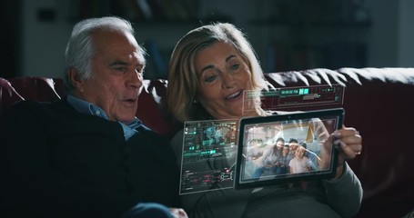 Close up of happy senior couple is making a video call to relatives with a futuristic tablet with the latest advanced augmented reality holographic technology in living room at home. - Powered by Adobe