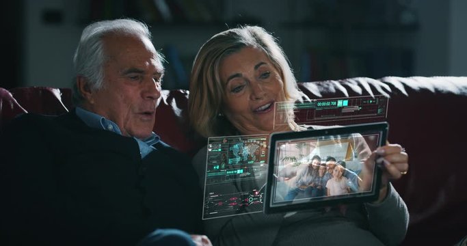 Close up of happy senior couple is making a video call to relatives with a futuristic tablet with the latest advanced augmented reality holographic technology in living room at home.