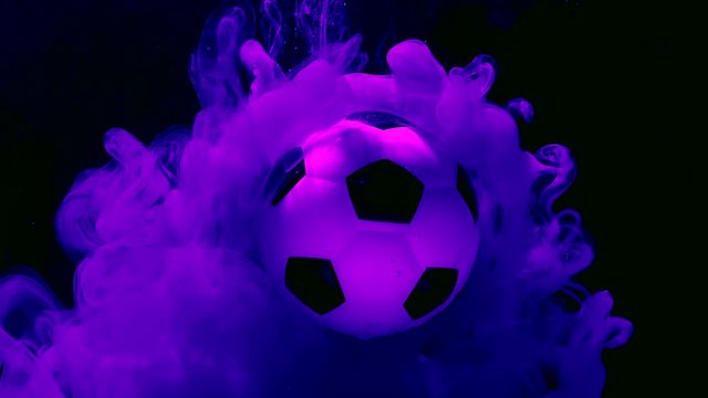 Soccer ball on amazing space background. Purple and pink ink in water on a dark blue background. Concept of advertising football competition. Fantastic screensaver.