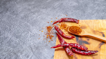 Cayenne pepper in a wooden spoon and dried chillies placed on a wooden chopping board on the cement floor