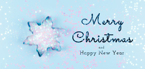 Flatlay with snowflake cookie cutter and snowflake sprinkles on blue background. Holiday, Christmas and New Year concept. Horizontal, wide screen banner format with Seasonal greetings