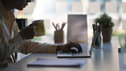 Cropped shot businessman holding coffee and using laptop computer.